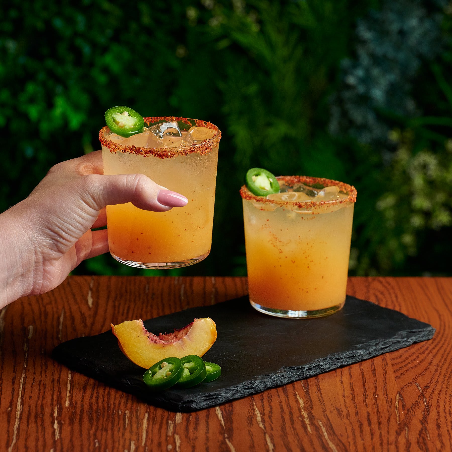 A hand holds two glasses of orange margaritas with jalapeño slices and peach garnishes in Atlanta, Georgia.