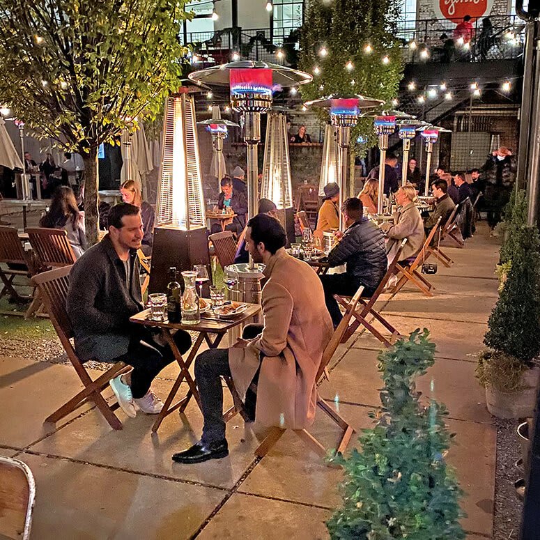 Outdoor restaurant patio with people dining at tables under string lights and patio heaters in Atlanta, Georgia.