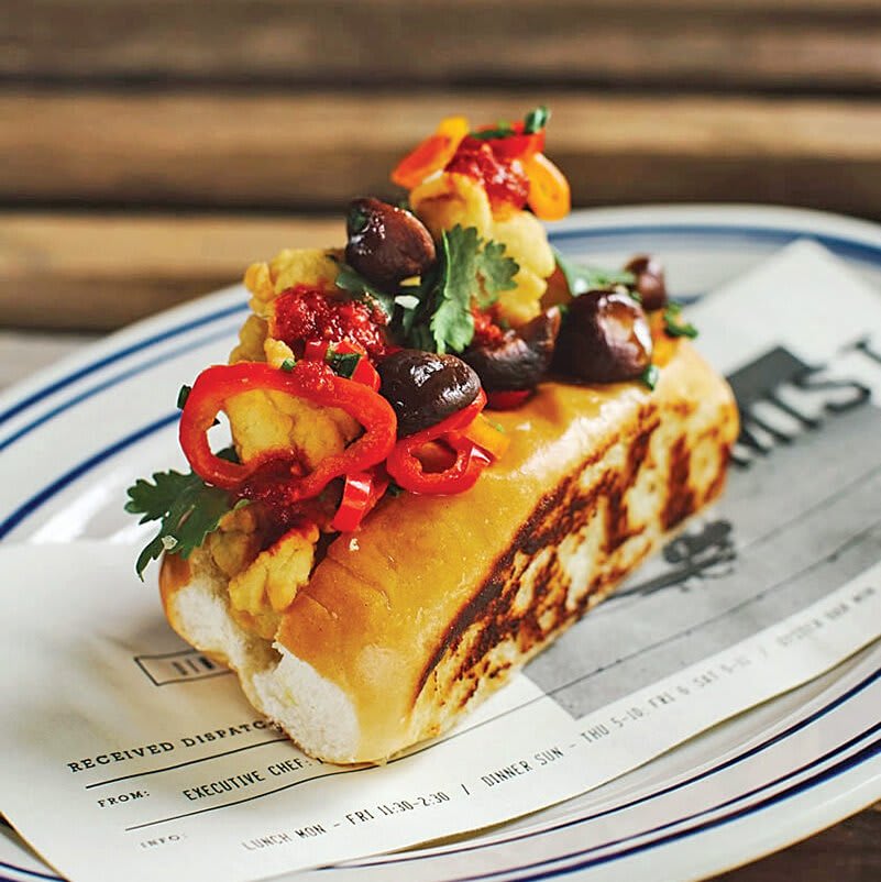 A gourmet hot dog with crispy fried chicken, mushrooms, and colorful peppers on a toasted bun in Atlanta, Georgia.