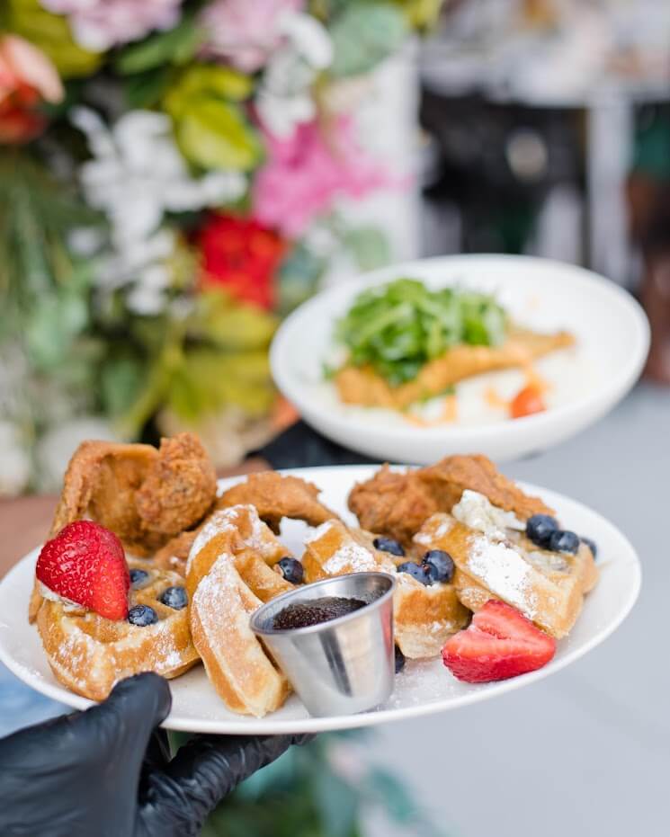 A plate of waffles topped with fried chicken, strawberries, blueberries, and syrup, with a side salad in Atlanta, Georgia.