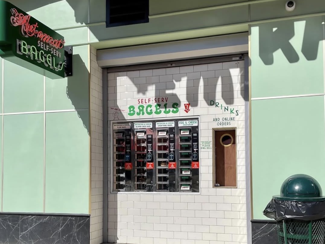 A green and white self-serve bagel and drink vending machine with a trash can nearby in Atlanta, Georgia.