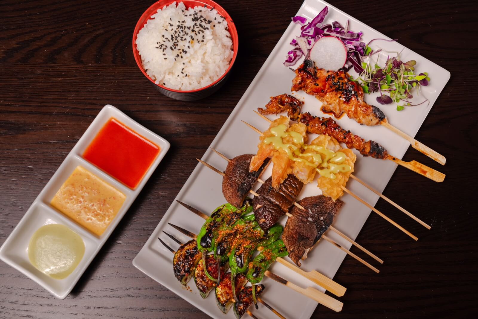Assorted grilled skewers with rice and dipping sauces on a dark wooden table in Atlanta, Georgia.