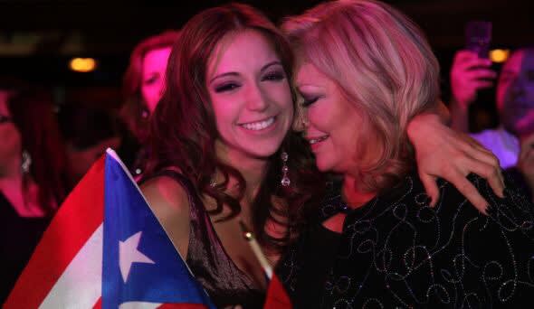 Laura Alemán 2 Two women embrace joyfully, one holding a Puerto Rican flag in Atlanta, Georgia.