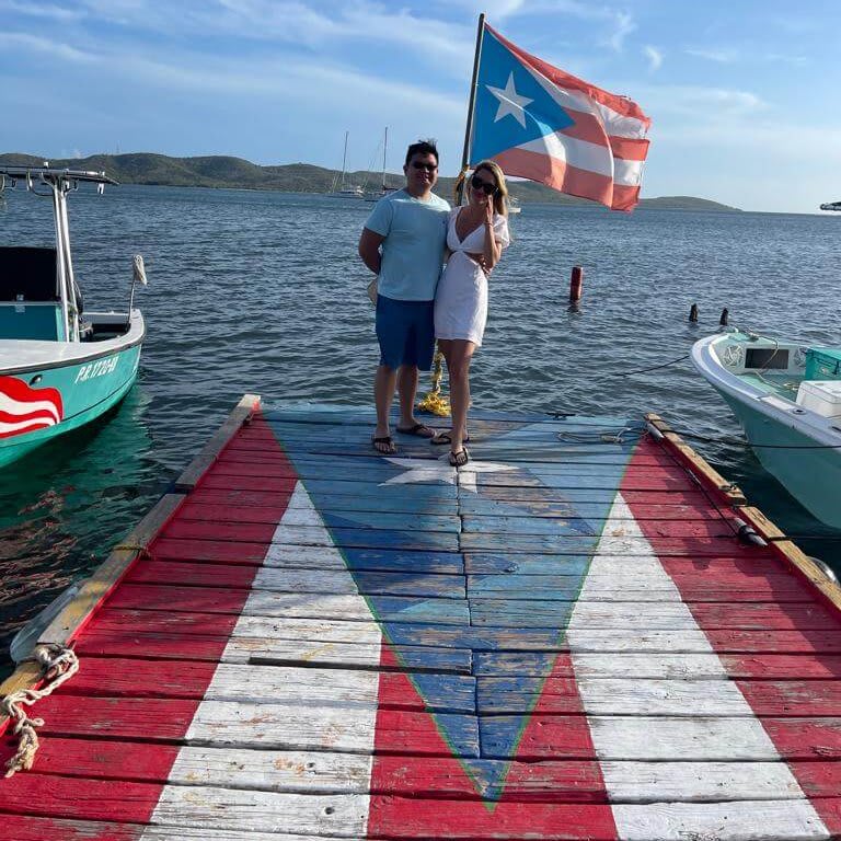 Couple stands on Puerto Rican flag-painted dock with boats and water in background in Atlanta, Georgia.
