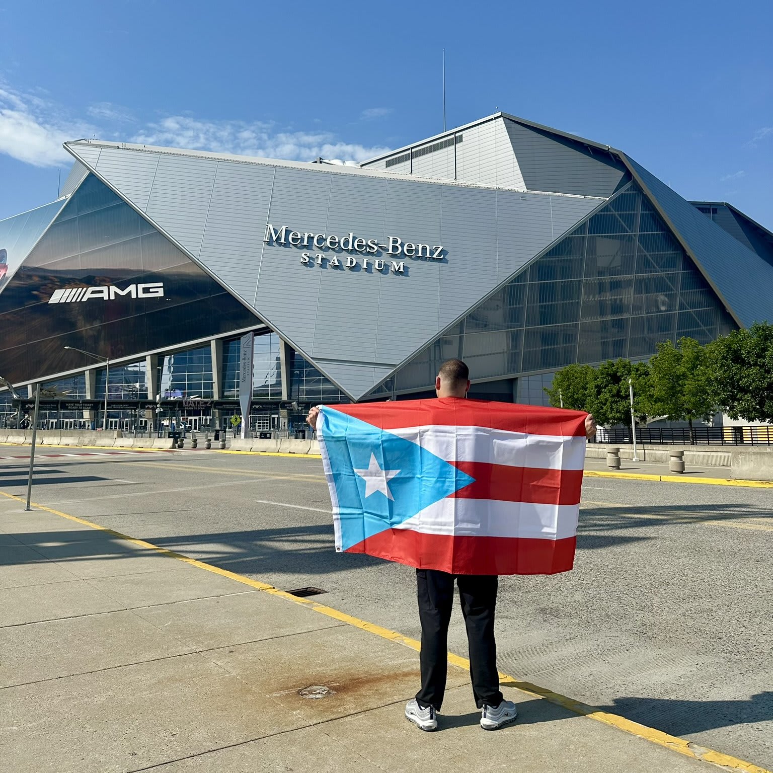 A man stands in front of Mercedes-Benz Stadium holding a Puerto Rican flag in Atlanta, Georgia.