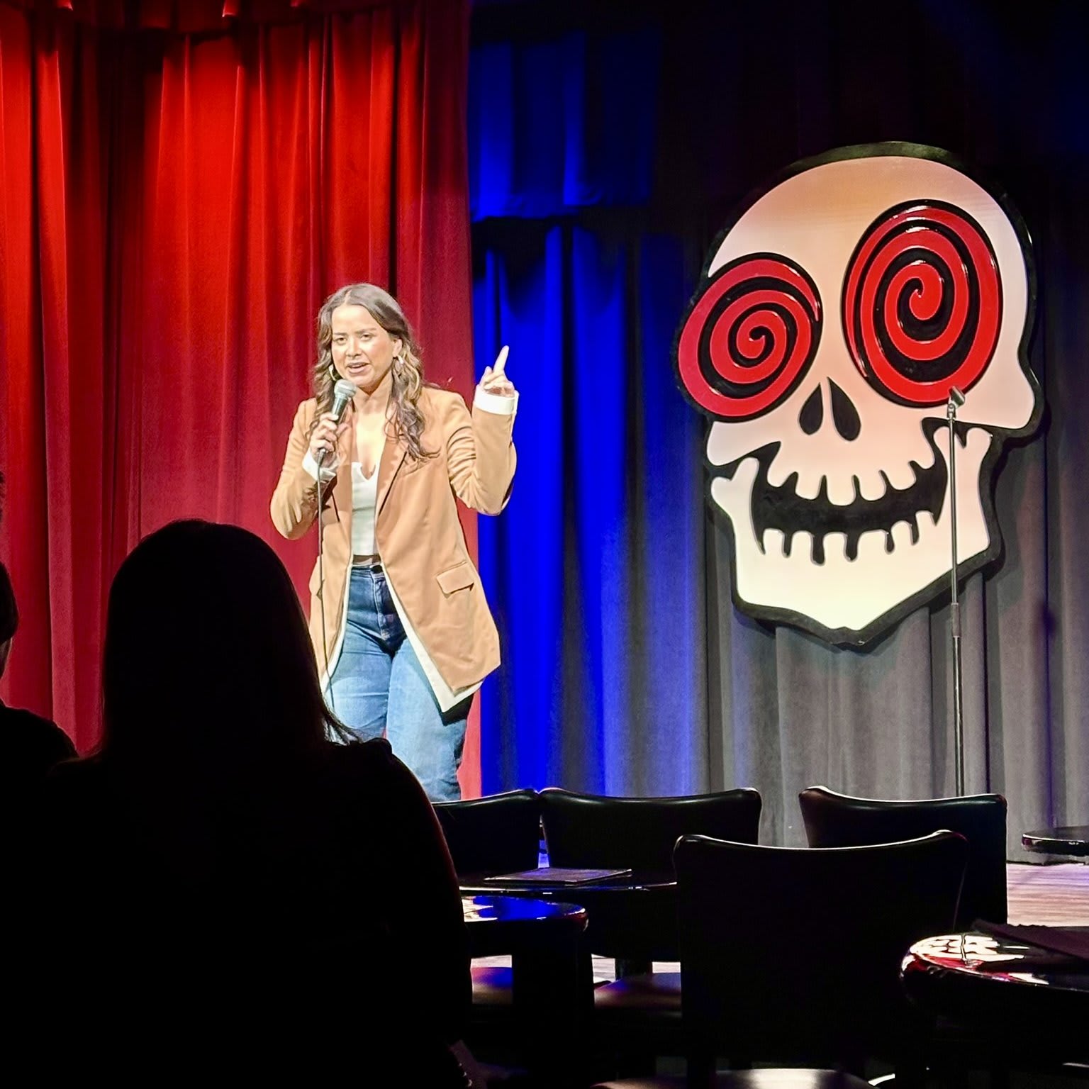 A woman in a brown jacket stands on stage with a microphone, addressing an audience in Atlanta, Georgia.