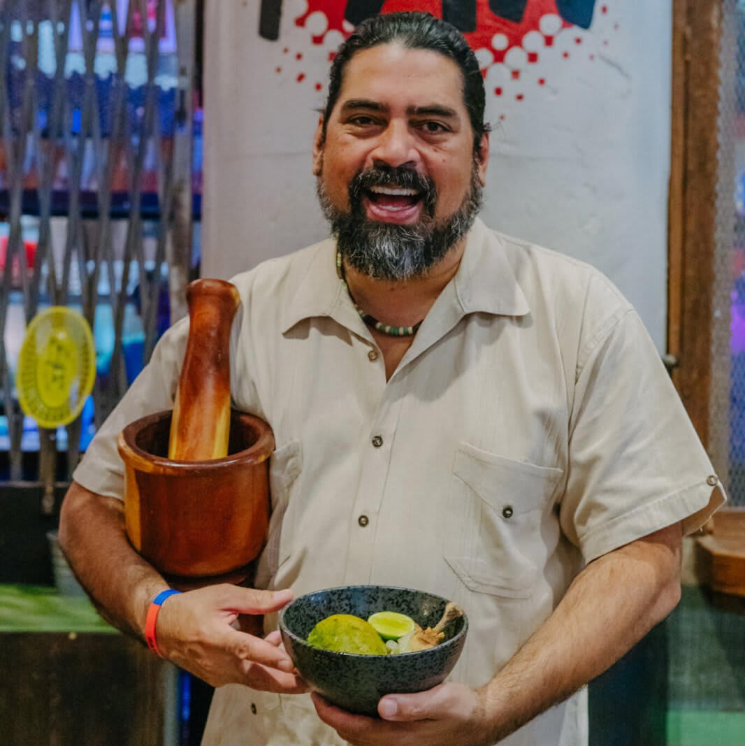 A smiling man with a beard holds a bowl of green sauce and a wooden pestle in Atlanta, Georgia.