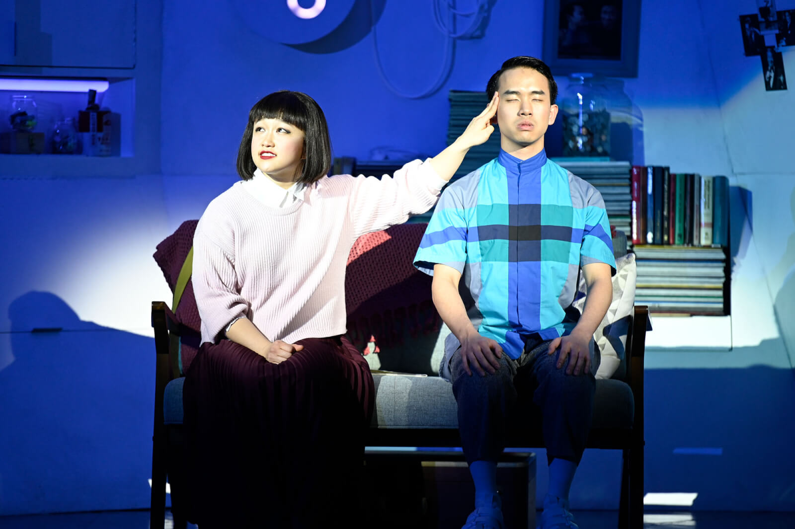 A man and woman sit on a couch, the woman touching the man's head in a dramatic pose in Atlanta, Georgia.