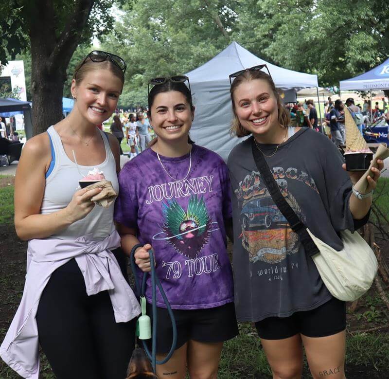 Three young women smile at the camera while holding ice cream cones at an outdoor event in Atlanta, Georgia.