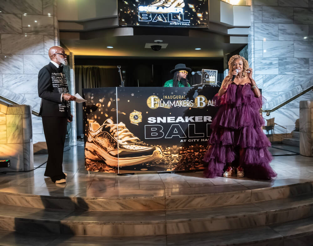 A man and woman stand on a stage at a formal event, with a large sneaker graphic behind them in Atlanta, Georgia.