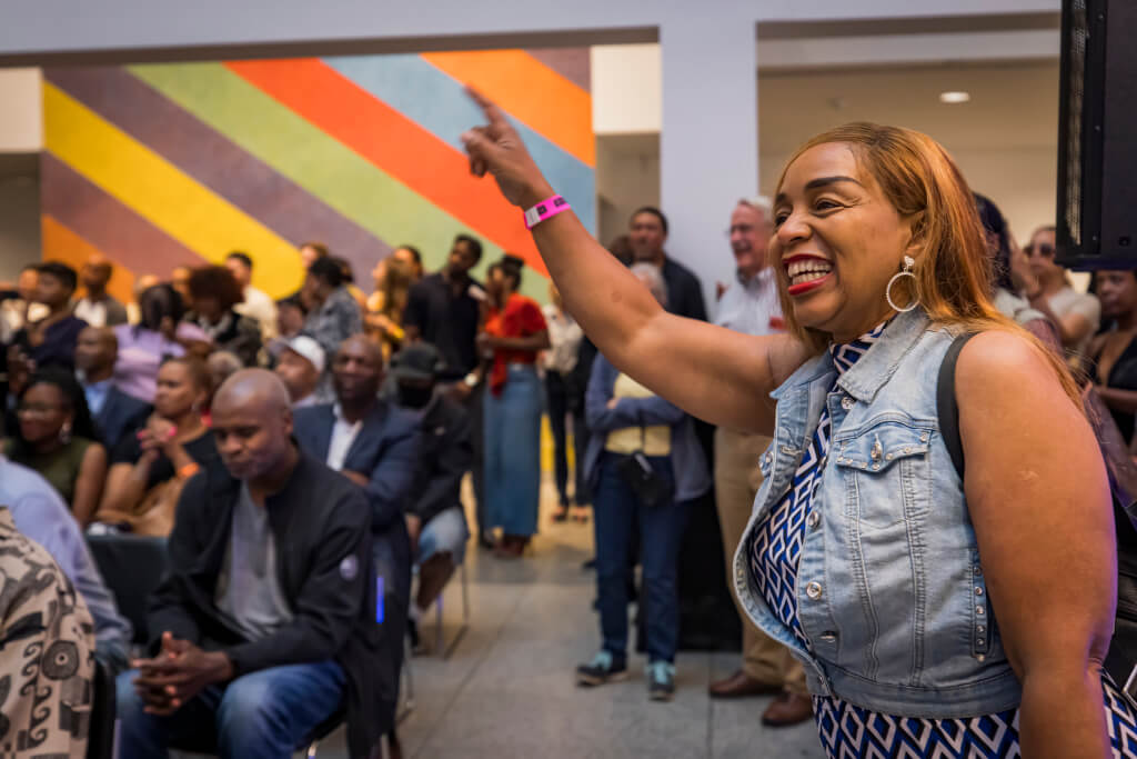 A woman in a denim vest raises her arm in a crowd, smiling broadly in Atlanta, Georgia.
