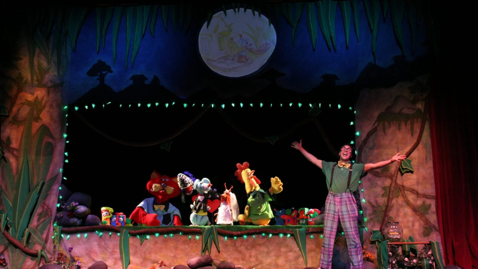 A lively puppet show featuring colorful characters on a jungle-themed stage with a moonlit backdrop in Atlanta, Georgia.