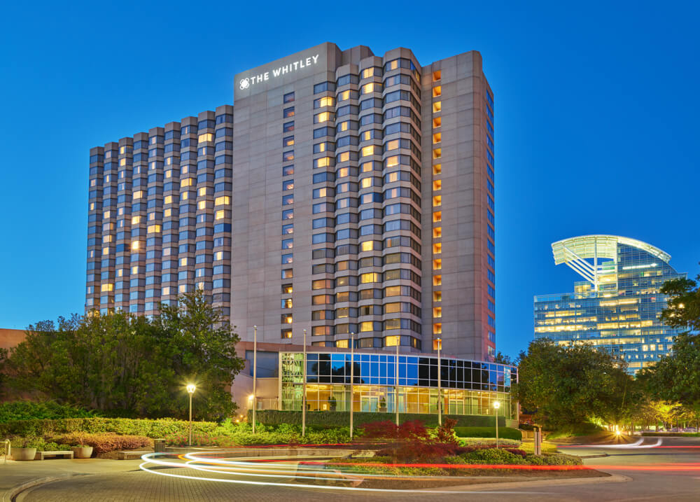 A modern hotel with a curved glass entrance and illuminated windows stands tall against the night sky in Atlanta, Georgia.