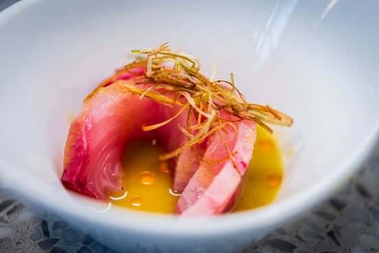 A white bowl contains thinly sliced raw fish with a yellow sauce and green garnish in Atlanta, Georgia.
