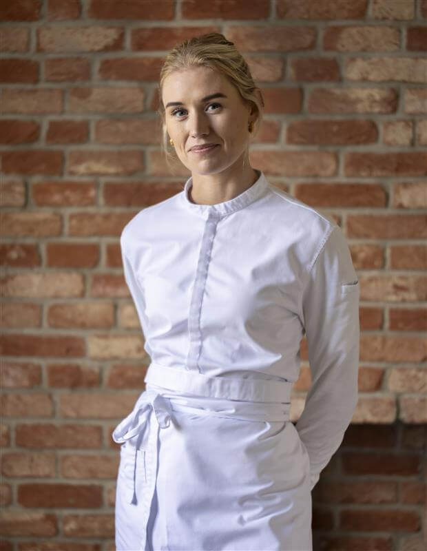 A woman in a white chef's uniform stands against a brick wall in Atlanta, Georgia.