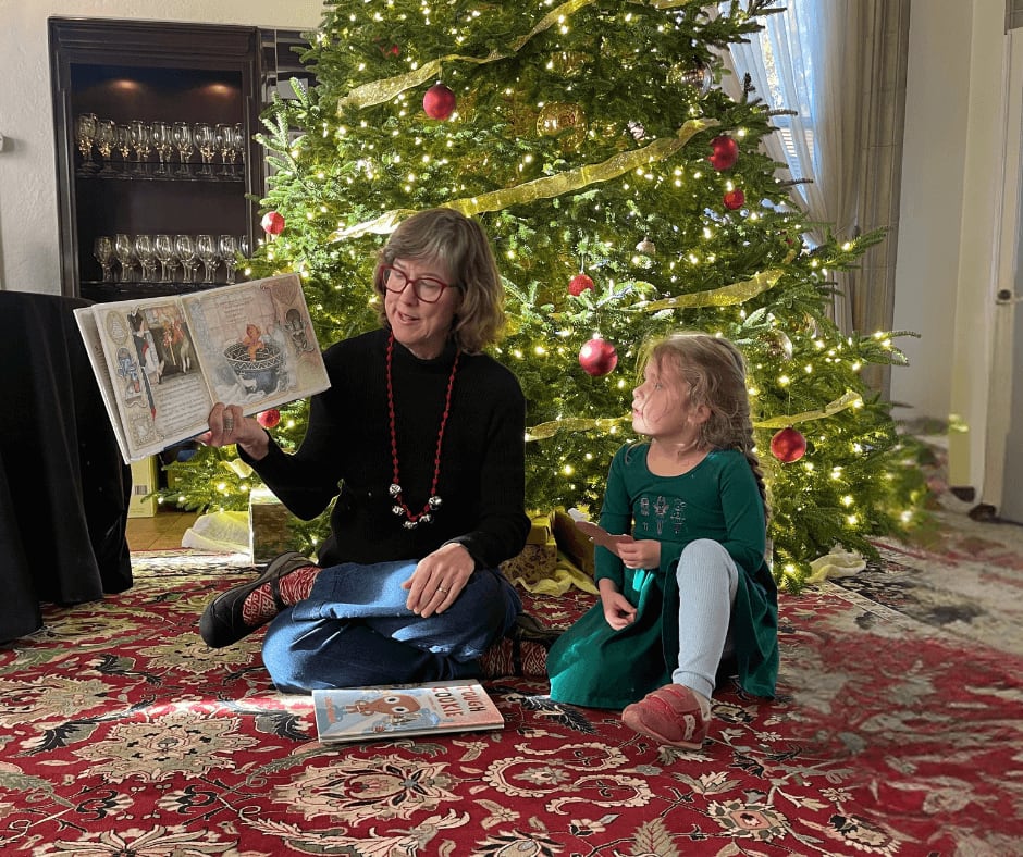 Cool Things to Do in November in Atlanta 11 A woman and young girl sit on a red rug reading a book together in front of a decorated Christmas tree in Atlanta, Georgia.