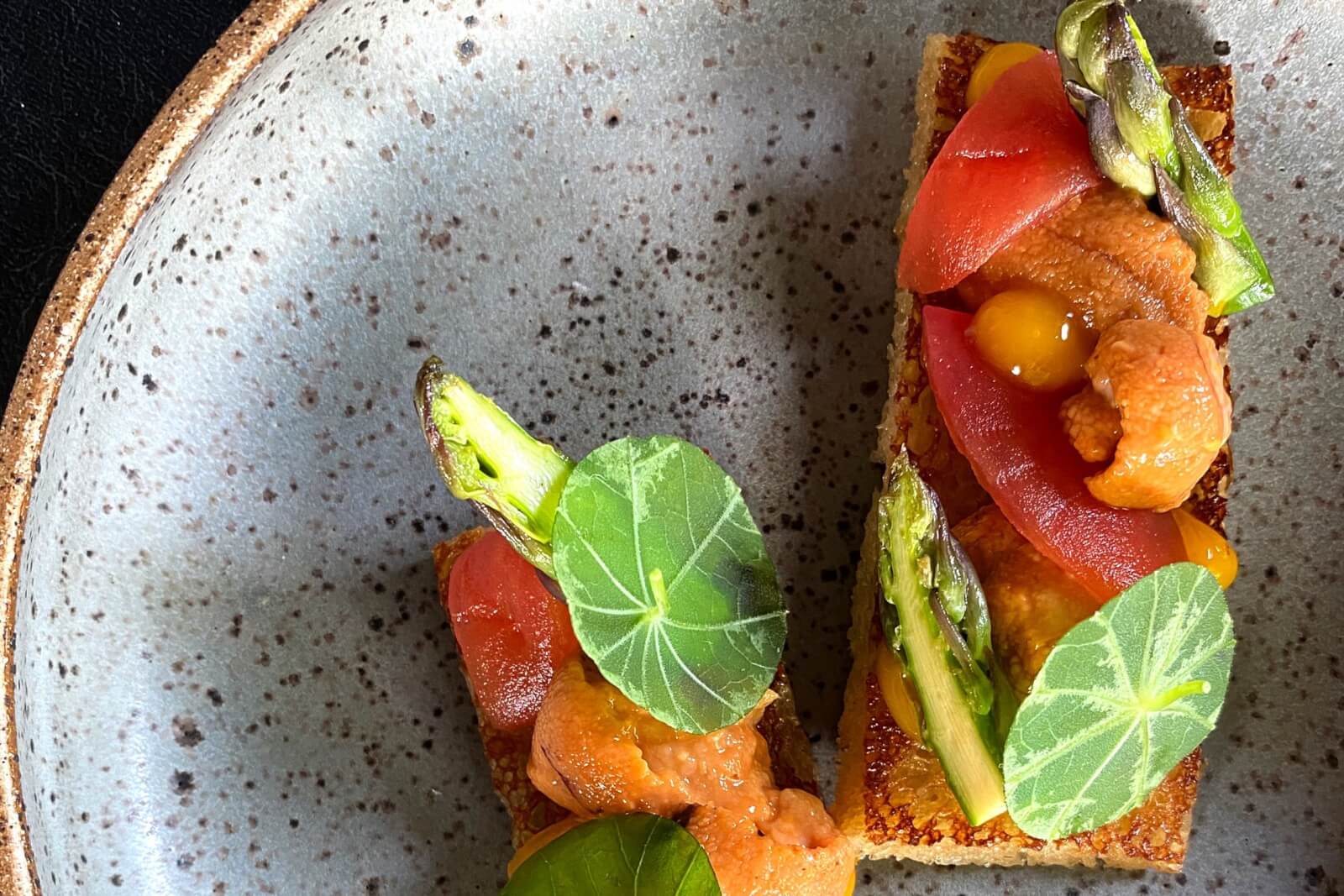 Two pieces of toast topped with orange roe, asparagus, tomatoes, and greens on a speckled plate in Atlanta, Georgia.