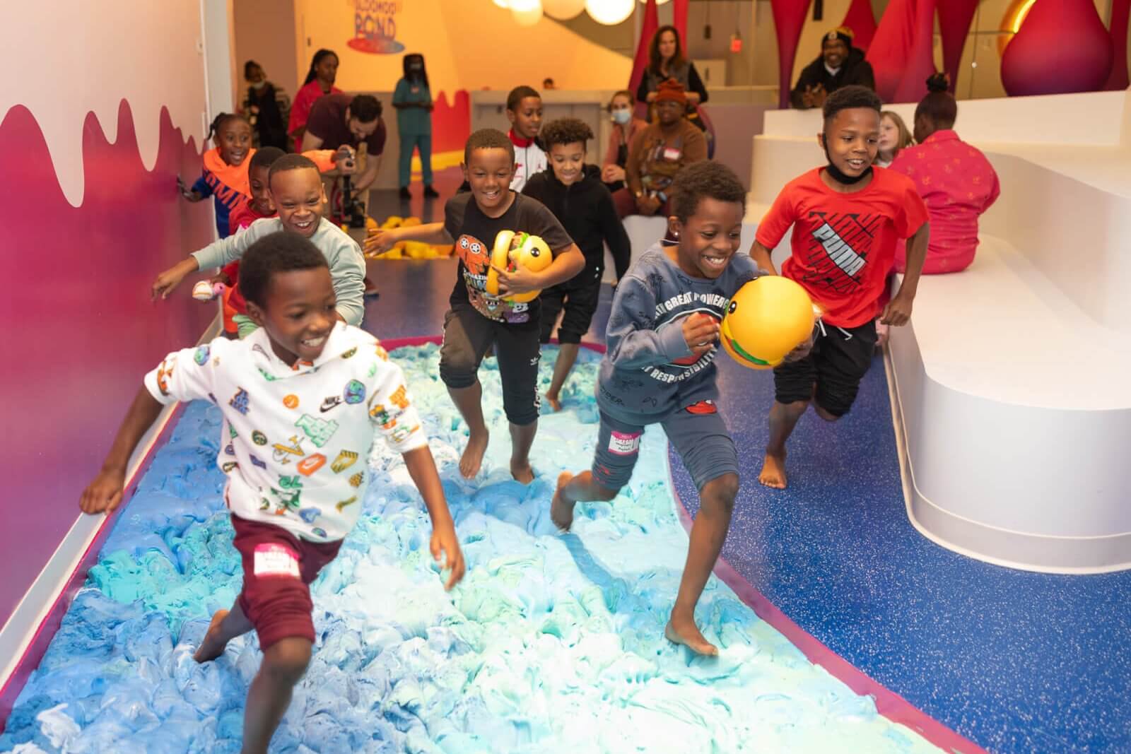 Children run barefoot through a colorful indoor play area with foam and balls in Atlanta, Georgia.