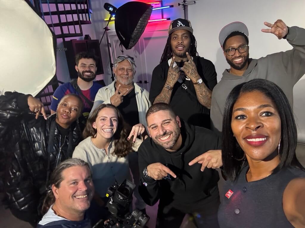 A diverse group of people, including a cameraman, pose together in a studio setting in Atlanta, Georgia.