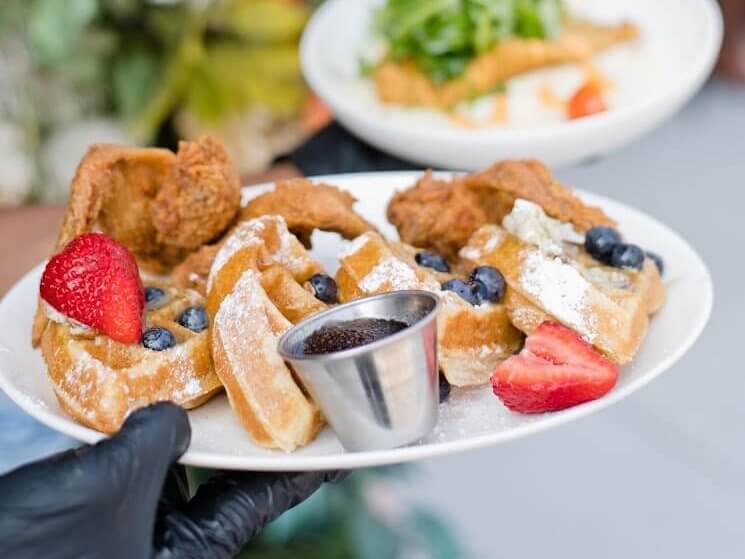A plate of waffles topped with fried chicken, strawberries, blueberries, and syrup, with a side salad in Atlanta, Georgia.