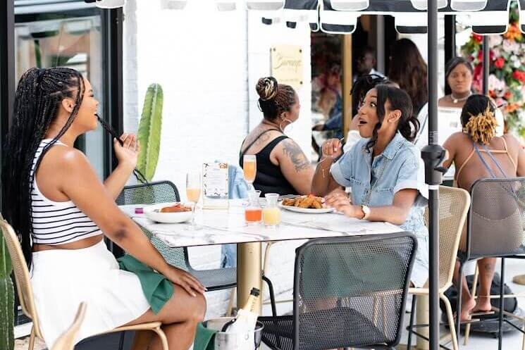Women enjoying a meal at an outdoor cafe with striped umbrellas and potted plants in Atlanta, Georgia.