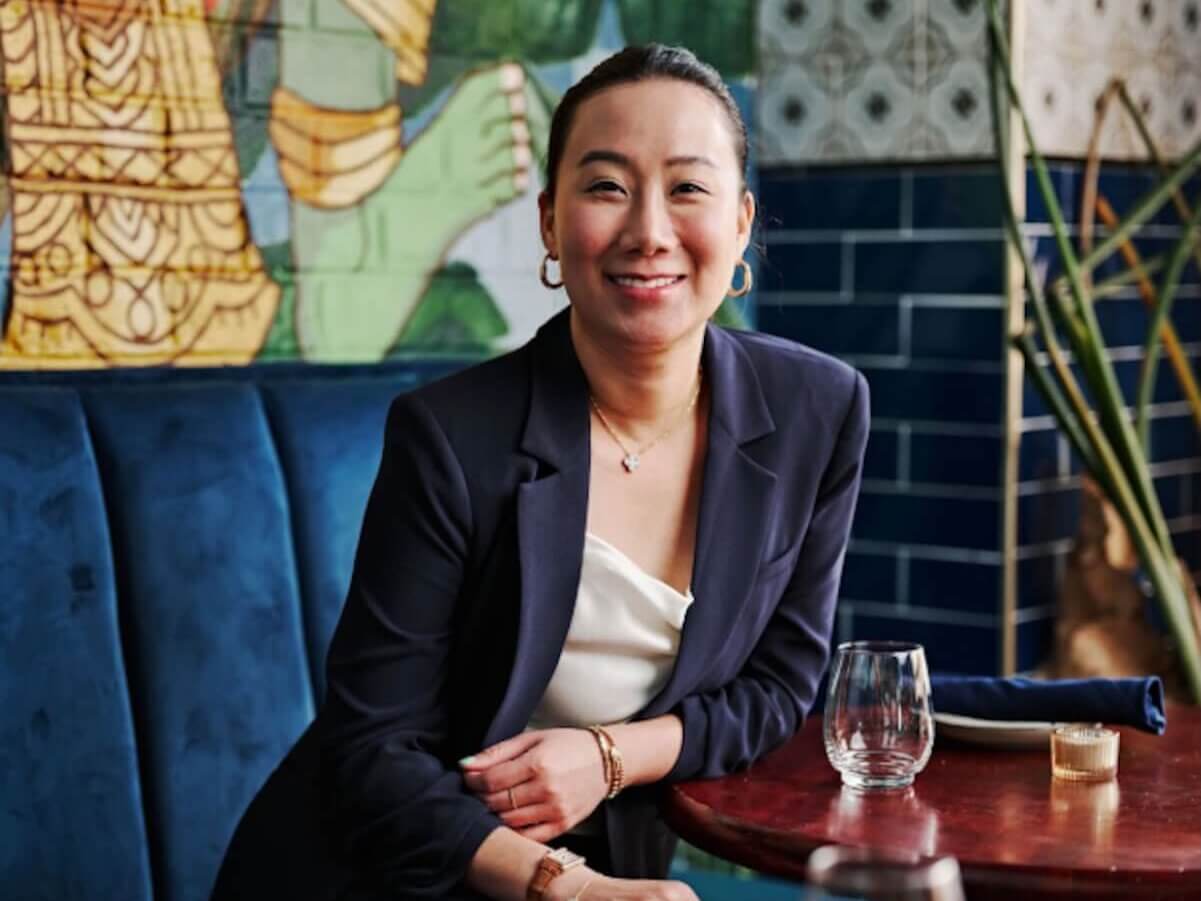 A woman in a navy blue blazer and white blouse sits smiling at a restaurant table with a colorful mural in the background in Atlanta, Georgia.