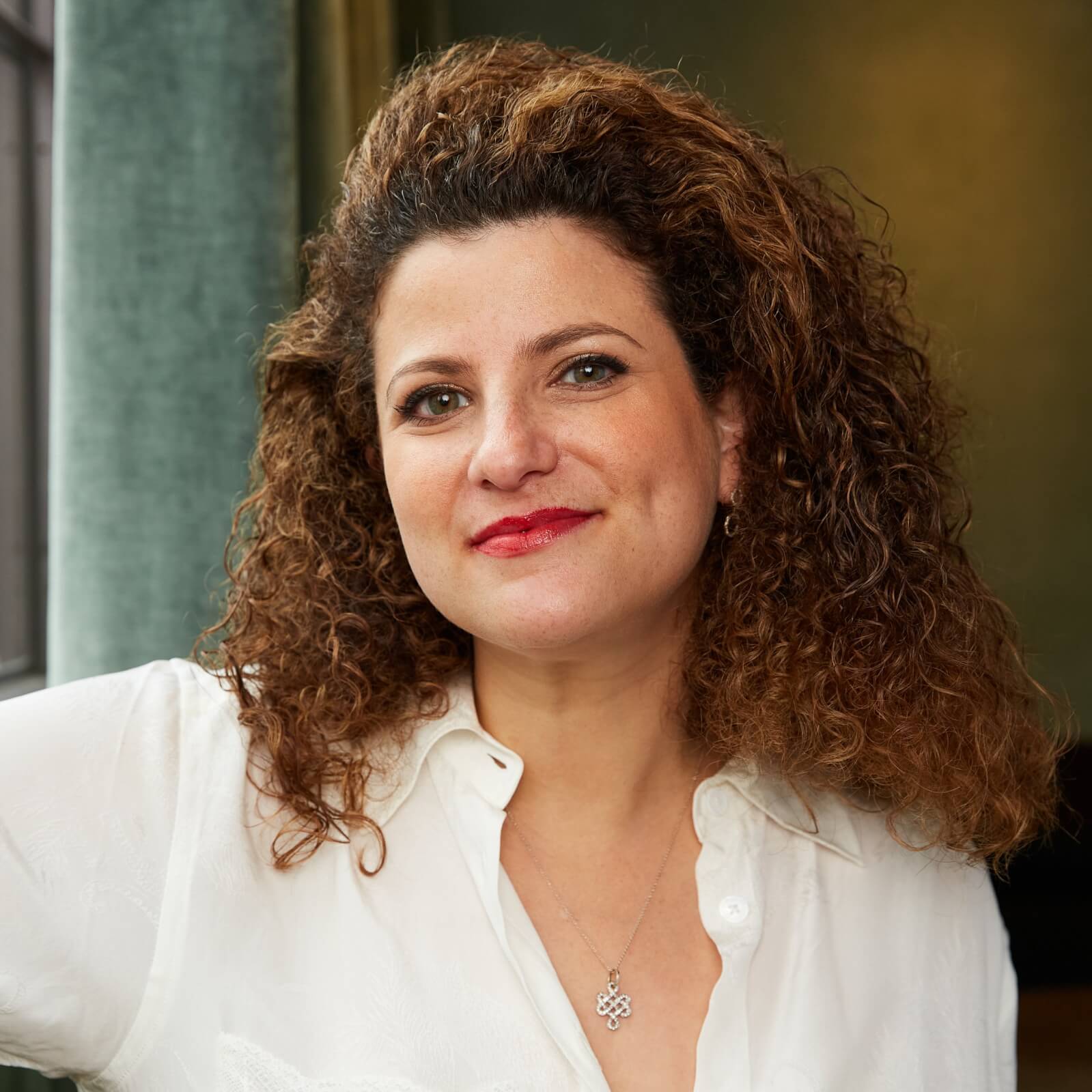 A smiling woman with curly hair wearing a white blouse stands indoors in Atlanta, Georgia.