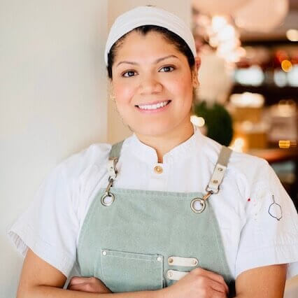 A smiling chef wearing a white hat and apron stands confidently with arms crossed in Atlanta, Georgia.