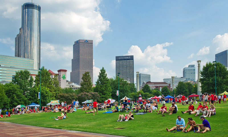 A vibrant city park filled with people enjoying a sunny day, surrounded by skyscrapers in Atlanta, Georgia.