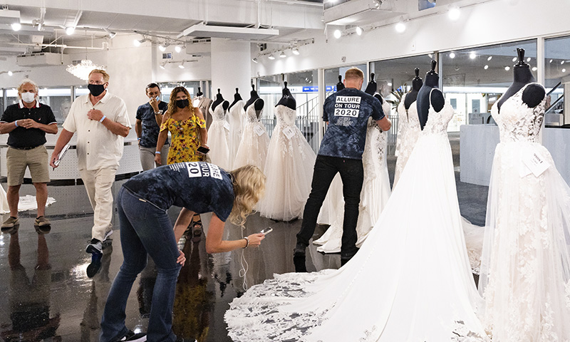 A group of people, some wearing masks, are trying on and photographing white wedding dresses in a bridal shop in Atlanta, Georgia.