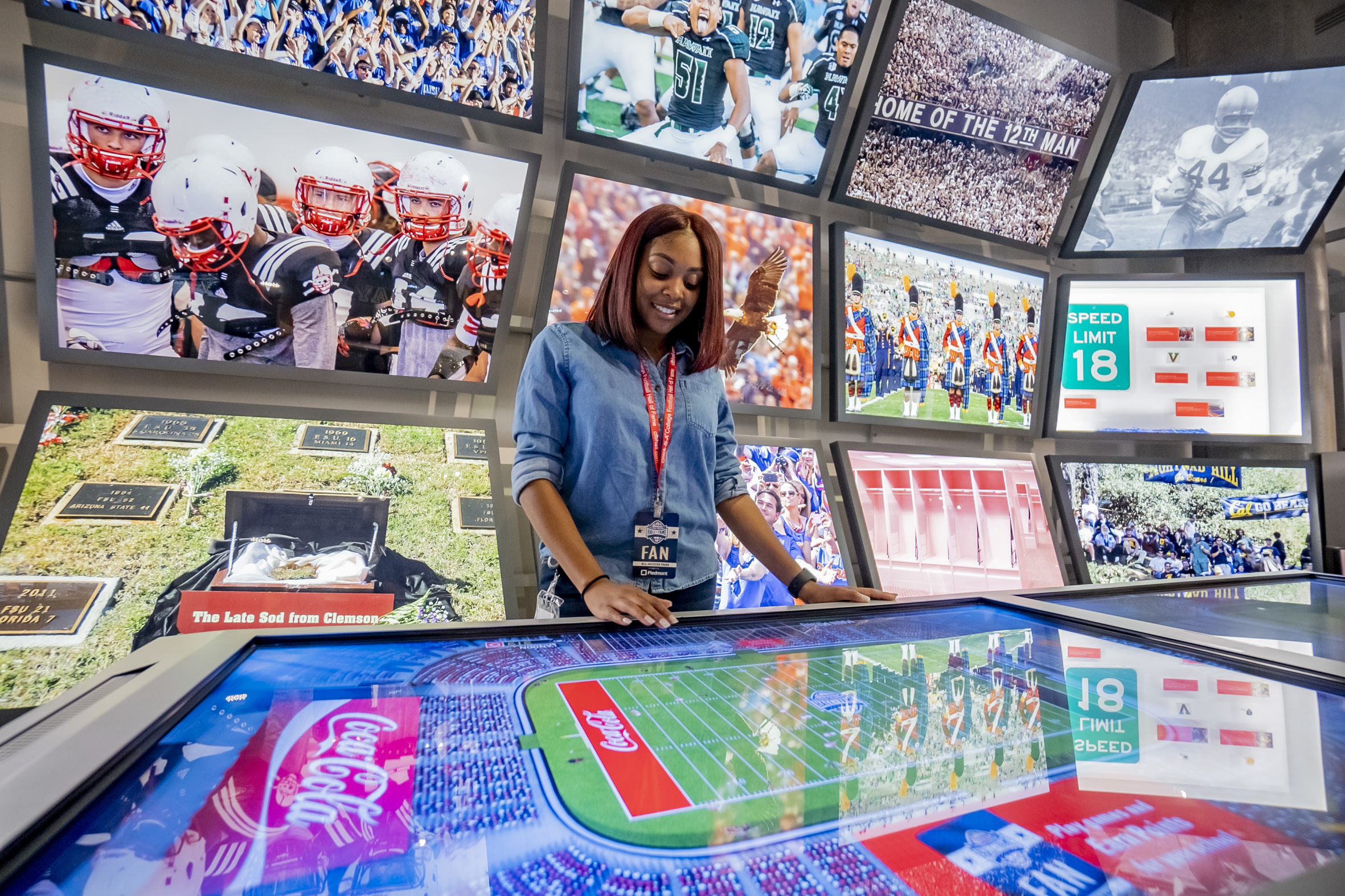 Woman standing in the middle of a room with televisions everywhere with football images.