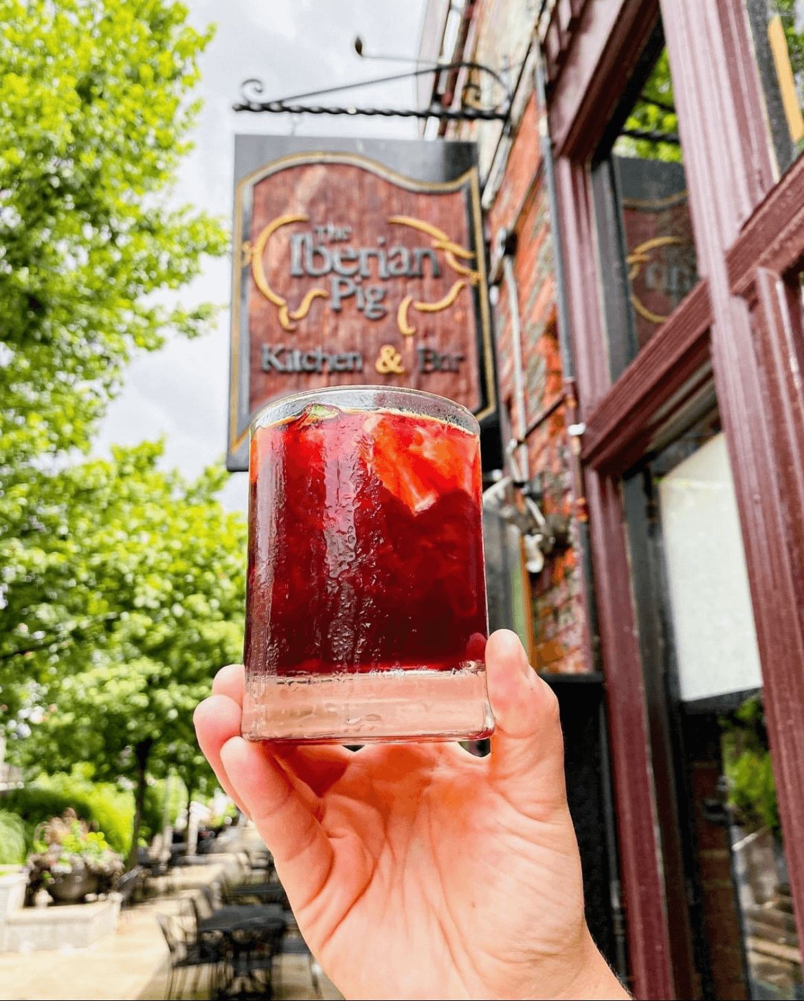 A hand holds a frosty glass of dark red sangria with fruit, outside a restaurant in Atlanta, Georgia.