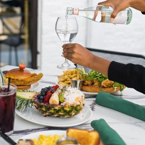 A person pours water into a wine glass at a table with various foods and drinks in Atlanta, Georgia.