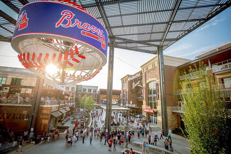 A bustling outdoor mall with a large baseball-themed sculpture and many people shopping and dining in Atlanta, Georgia.