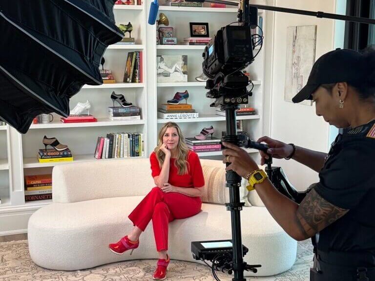 Woman in red outfit sits on white couch while being filmed by camera operator in Atlanta, Georgia.