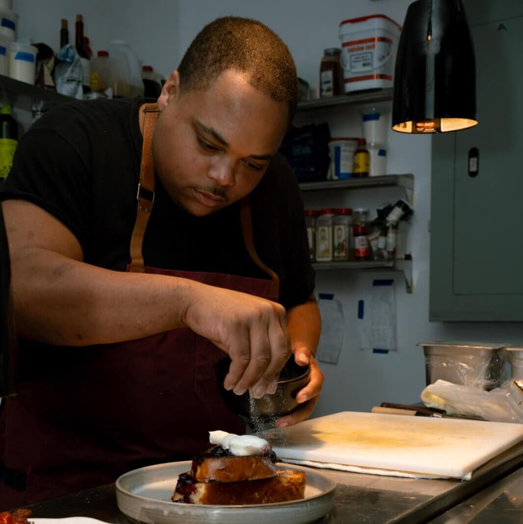 A chef in a kitchen carefully sprinkles sugar on a dessert, focusing intently on the task at hand in Atlanta, Georgia.