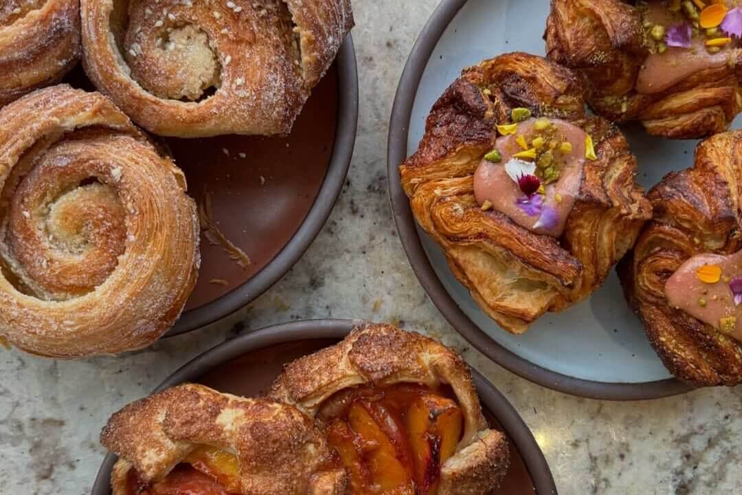 Assorted pastries including cinnamon swirls, pistachio and rose water pastries, and peach tarts arranged on plates on a marble countertop in Atlanta, Georgia.