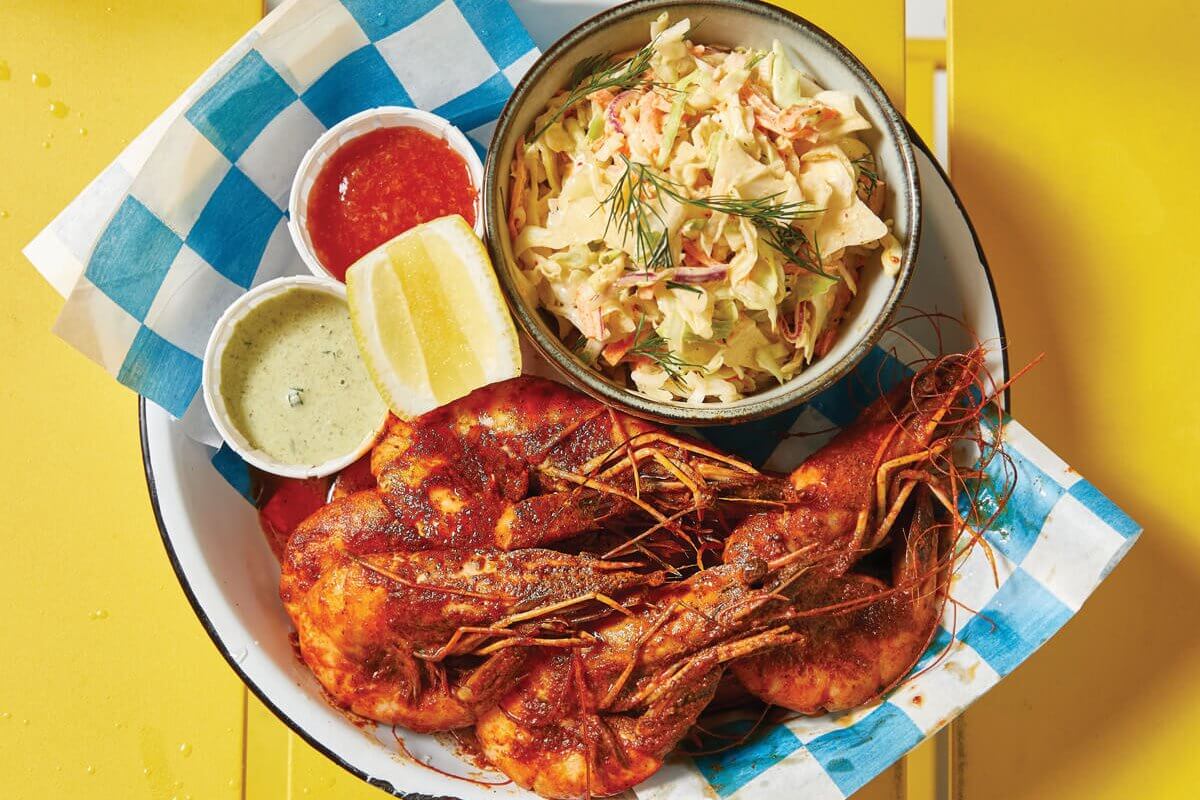 A vibrant plate of spicy fried shrimp served with coleslaw, lemon wedges, and three dipping sauces on a yellow table in Atlanta, Georgia.