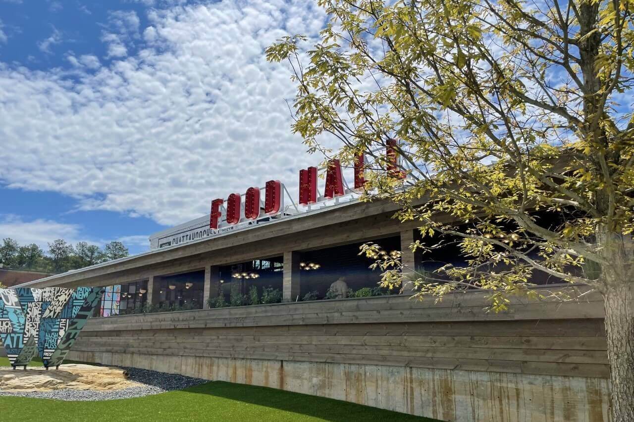 A modern building with a large red 'FOOD HALL' sign and a green roof, surrounded by trees and grass in Atlanta, Georgia.