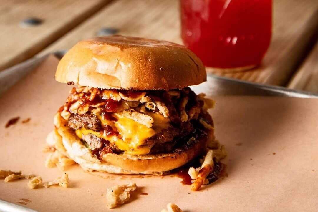 A mouthwatering BBQ cheeseburger with crispy onion strings and a tangy red drink in a mason jar in Atlanta, Georgia.