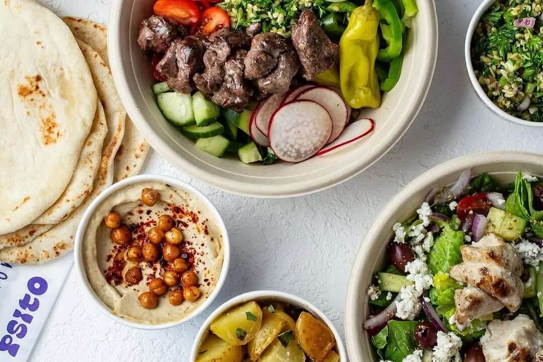 A variety of Mediterranean dishes including salads, hummus, pita bread, and roasted vegetables, all arranged on a white surface in Atlanta, Georgia.