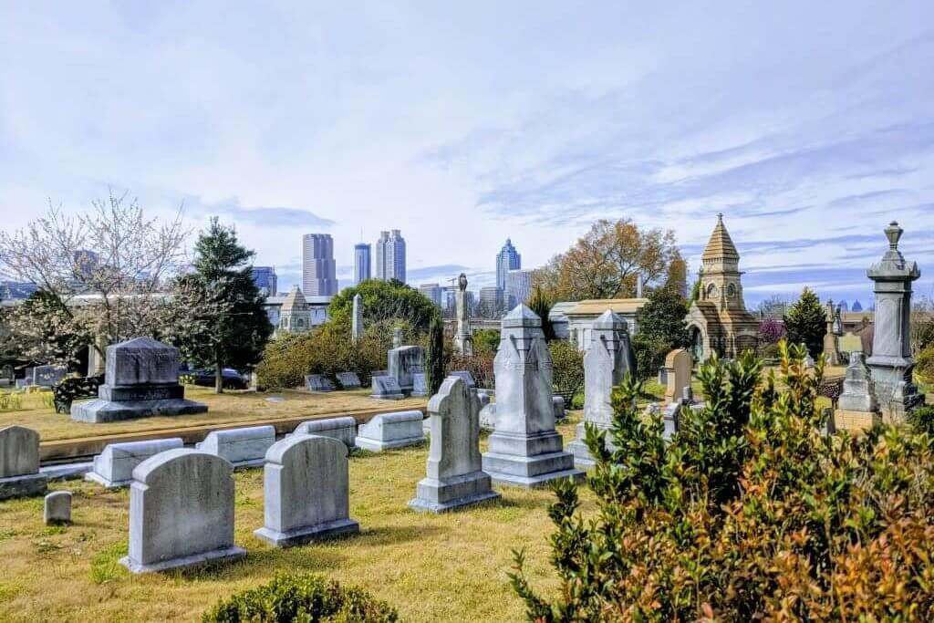 A serene cemetery with gravestones and mausoleums under a clear sky, with a city skyline in the distance in Atlanta, Georgia.