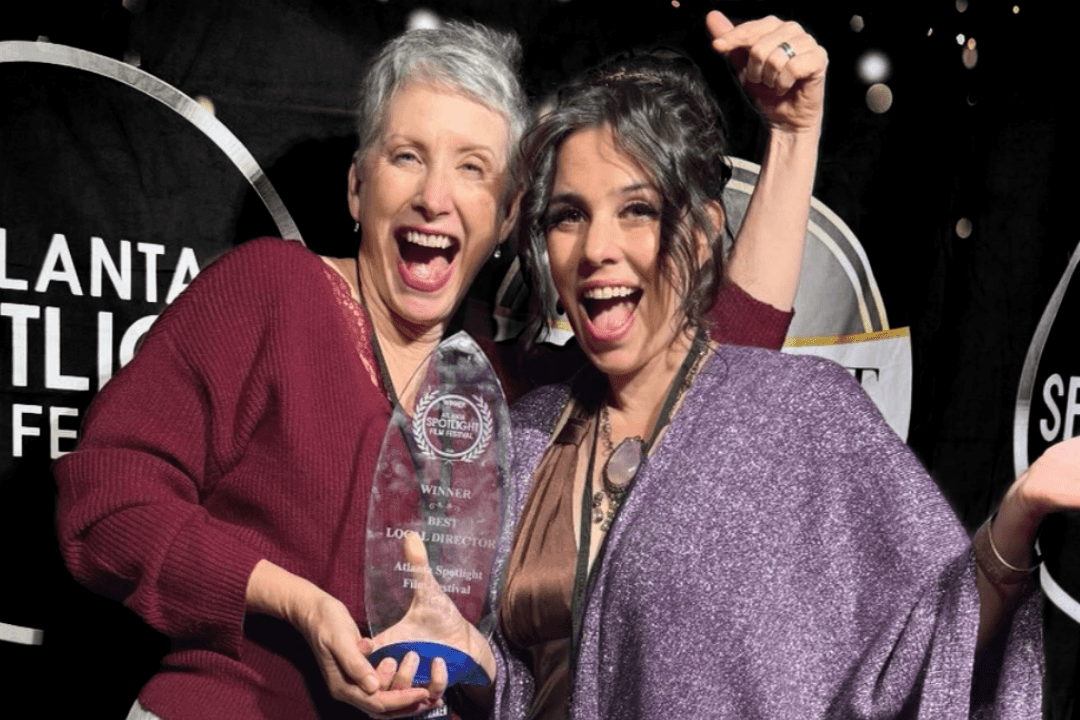 Two women joyfully celebrate their award win, holding a trophy together in front of a festive backdrop in Atlanta, Georgia.
