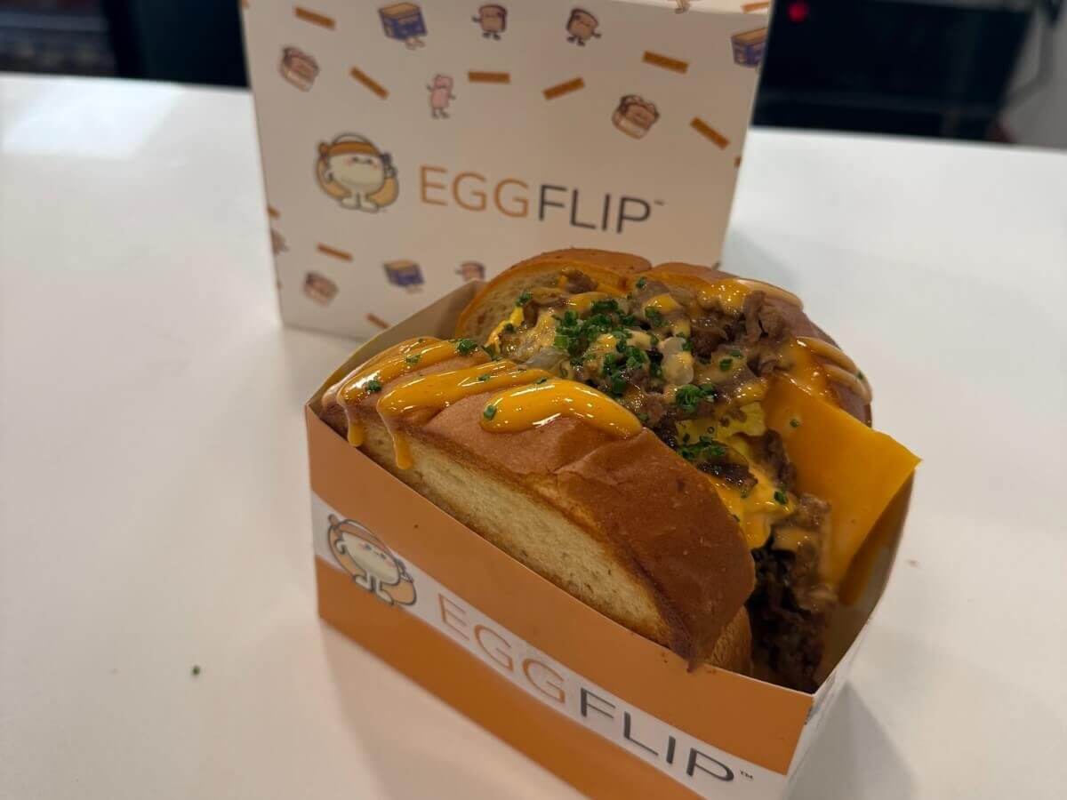 A mouthwatering Egg Flip burger with melted cheese, topped with a creamy sauce and chives, served in a branded orange box in Atlanta, Georgia.
