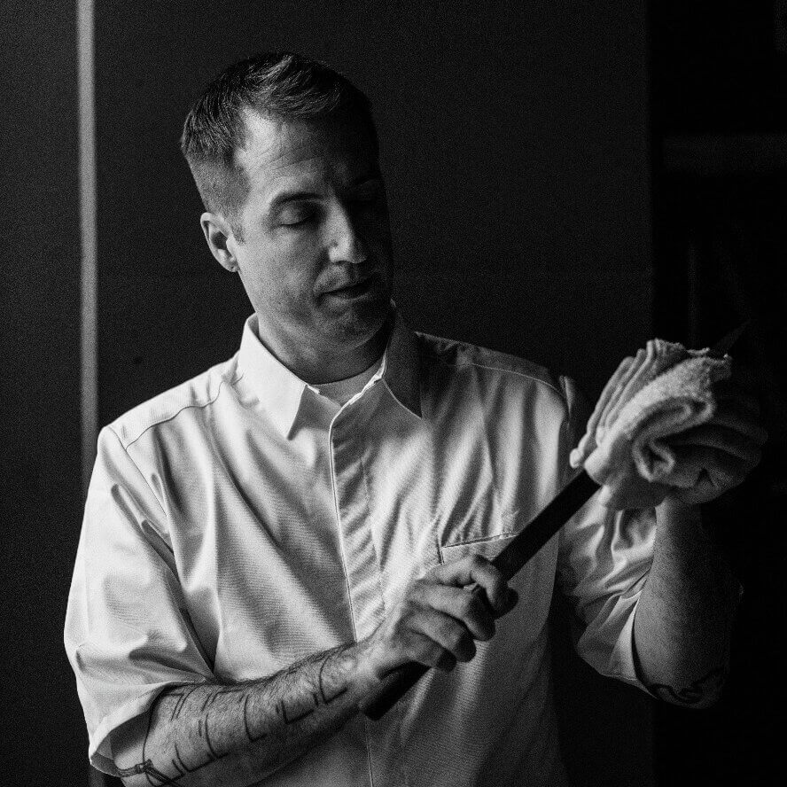 A chef in a white uniform carefully slices a piece of meat with a sharp knife in Atlanta, Georgia.