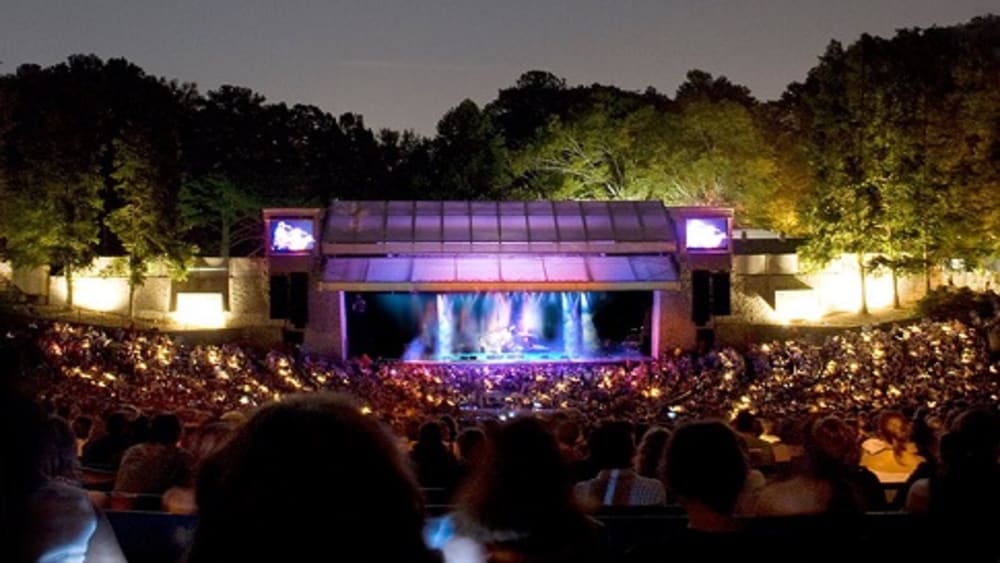 A large crowd gathers at an outdoor concert under the night sky, illuminated by stage lights in Atlanta, Georgia.