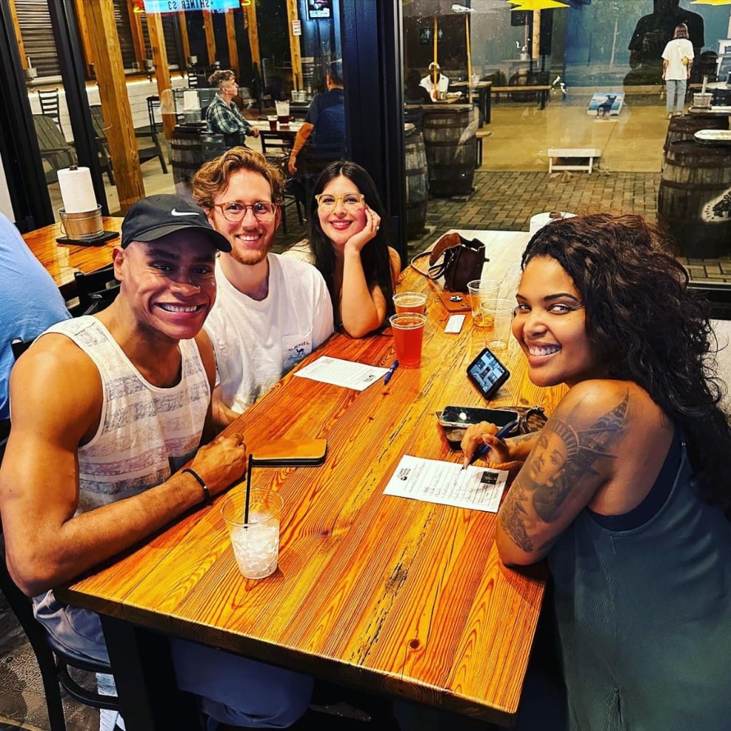 Four friends enjoying drinks and conversation at a wooden table in a casual outdoor setting in Atlanta, Georgia.