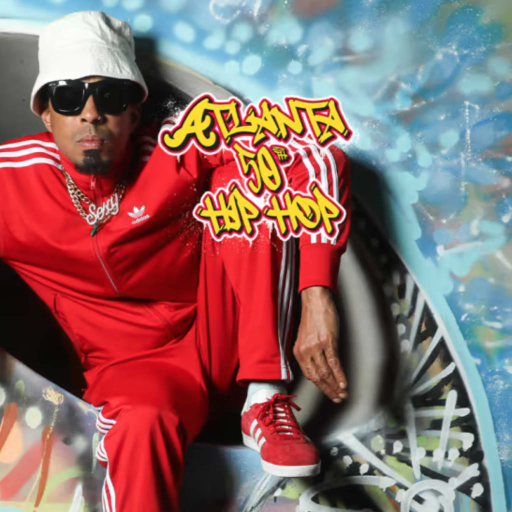 A man in a red tracksuit and bucket hat poses against a graffiti backdrop in Atlanta, Georgia.