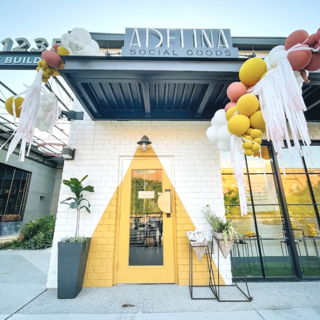 A vibrant storefront with a yellow door and balloon arch, advertising 'Adelina Social Goods' in Atlanta, Georgia.