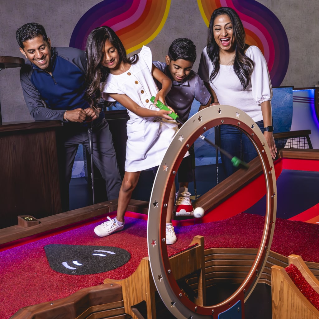 A family of four enjoys a mini-golf game, with a colorful, futuristic course and interactive elements in Atlanta, Georgia.